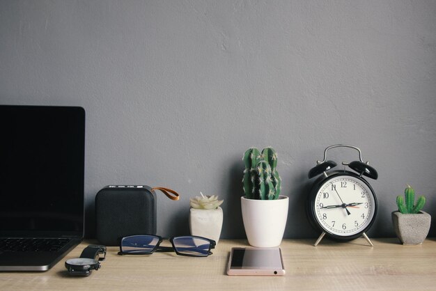 Wekker en planten op witte pot met kantoor- en persoonlijke accessoires op werktafel en grijze achterkant