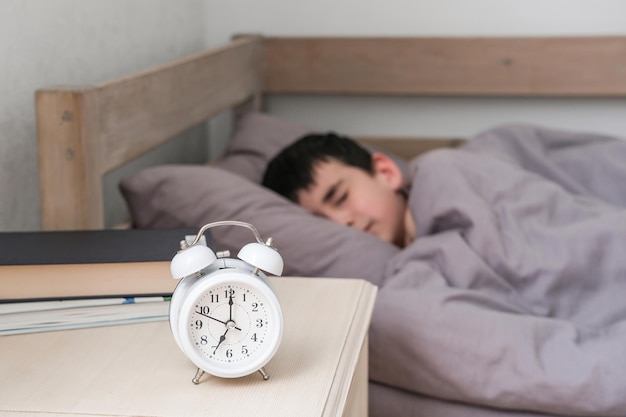 Wekker op het nachtkastje tegen de achtergrond van een jongen die onder een deken slaapt