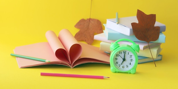 Wekker stapel boeken en briefpapier op gele achtergrond terug naar schoolvakanties