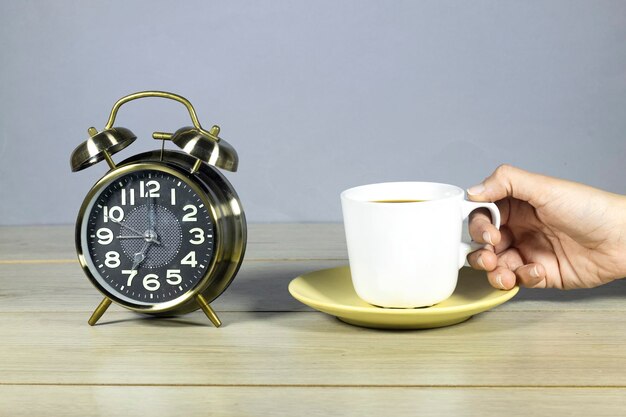 wekker wijst 7 uur met vrouwelijke hand drinkt een kop koffie klaar voor het werk concept