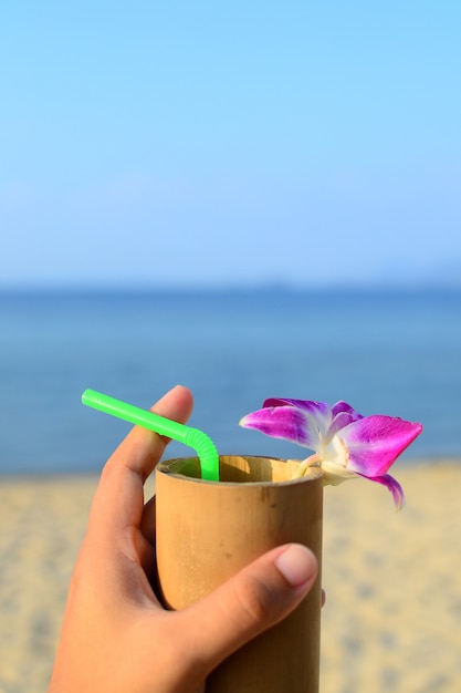 Foto bevanda di benvenuto con vetro di bambù e decorare con orchidea viola su sabbia, mare e cielo blu sullo sfondo.