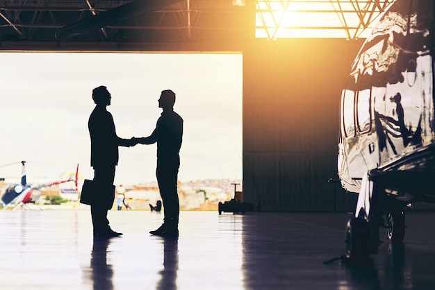 Welcome home Full length shot of two unrecognizable businessmen shaking hands while standing in a hanger at the airport