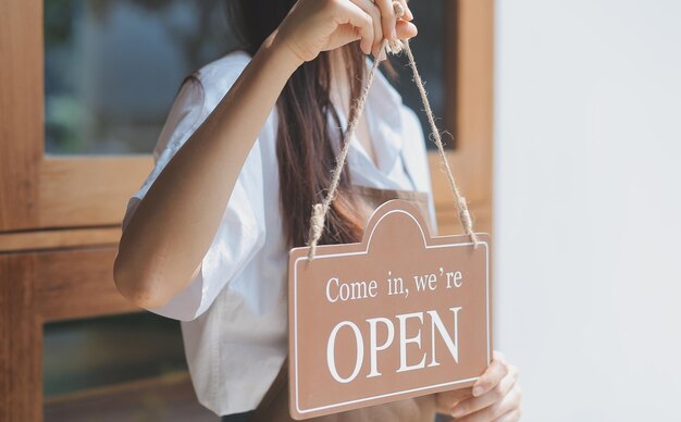 Foto benvenuto open barista cameriera donna che gira il cartello aperto sulla porta di vetro nella moderna caffetteria caffetteria pronta a servire bar ristorante negozio al dettaglio piccolo imprenditore cibo e bevande concetto