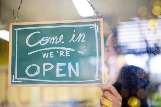 Welcome Open barista waitress woman turning open sign board on glass door