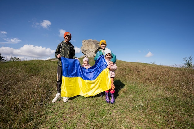 Welcome to Ukraine Four children hold ukrainian flag near big stone in hill Pidkamin