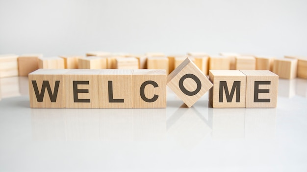 Welcome - word of wooden blocks with letters on a gray background. Reflection of the caption on the mirrored surface of the table. Selective focus.