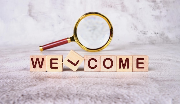 A WELCOME word written on wooden blocks with a magnifying glass in the background