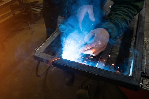 The welder cooks the frame. The welder cooks the metal. The welder cooks metal structures. Welding works. Sparks, molten metal