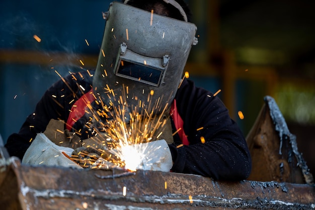 Welder in iron mask helmet welds steel welding industrial\
worker at the factory welding steel