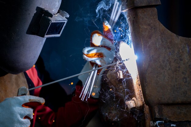 Welder in iron mask helmet welds with electric arc steel
welding industrial worker at the factory