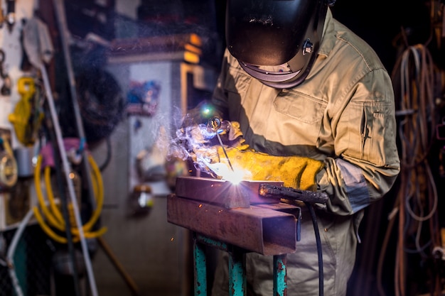 Welder last metalen onderdeel in fabriek. Lasser in beschermende uniforme en masker lassen metalen buis op de industriële