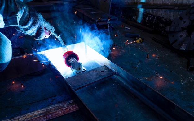 Welder welding metal with argon arc welding machine and has welding sparks a man wears gloves