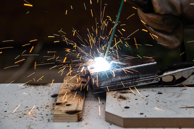 A welder welds a metal piece and sparks from welding fly in different directions