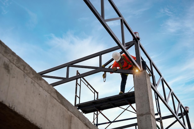 A 危険区域の溶接工 鉄骨屋根トラス溶接工は、建設現場での落下の安全を防止するための安全装置を備えた屋根構造に取り組んでいます