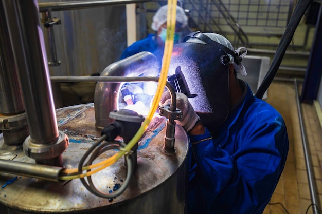Foto il metallo riparato maschio del lavoratore dell'argon dell'arco di saldatura sta saldando le scintille del tubo di riparazione della costruzione industriale inossidabile