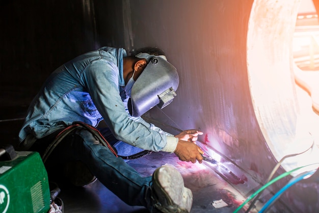 Foto il metallo riparato maschio del lavoratore dell'argon dell'arco di saldatura sta saldando l'olio del serbatoio della costruzione industriale delle scintille all'interno di spazi ristretti.