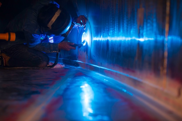 溶接アークアルゴン労働者の男性の修理された金属は、限られたスペース内で火花産業建設タンクのステンレス油を溶接しています。