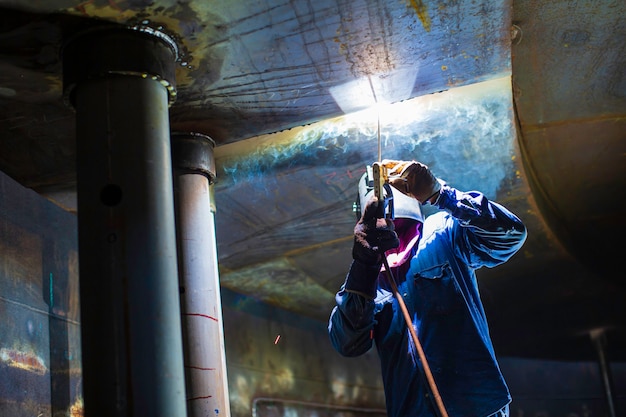 Foto l'arco metallico del lavoratore maschio di saldatura fa parte del serbatoio di stoccaggio di petrolio e gas per la costruzione di condutture di serbatoi di macchinari all'interno di spazi ristretti.