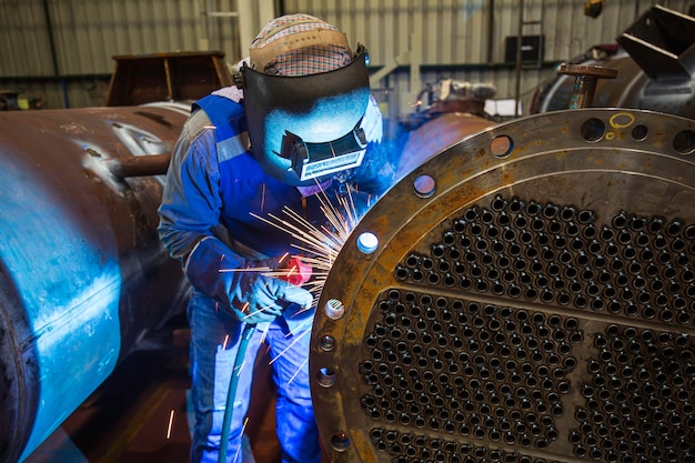 Foto la saldatura del metallo del lavoratore maschio fa parte della costruzione della conduttura della flangia di scambio termico del macchinario petrolio e gas