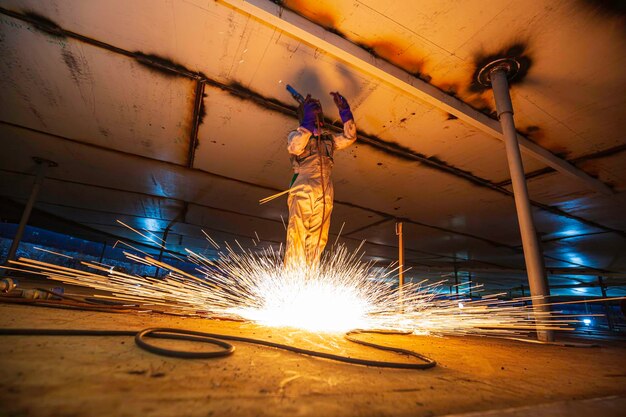 Welding male worker metal is part of machinery plate roof tank beam construction flash spark inside confined spaces