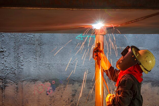 Welding male worker metal is part of machinery plate roof tank beam construction flash spark inside confined spaces