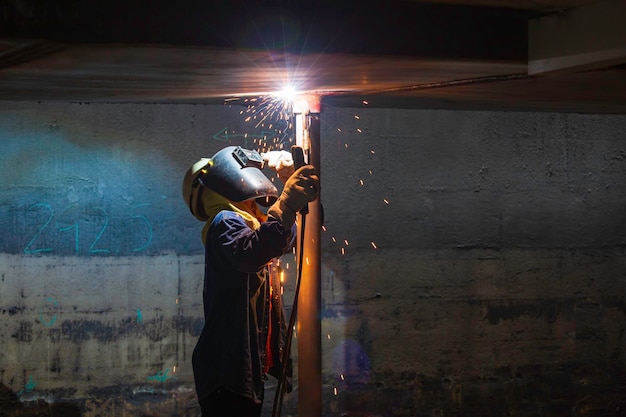 Welding male worker metal is part of machinery plate roof tank beam construction flash spark inside confined spaces