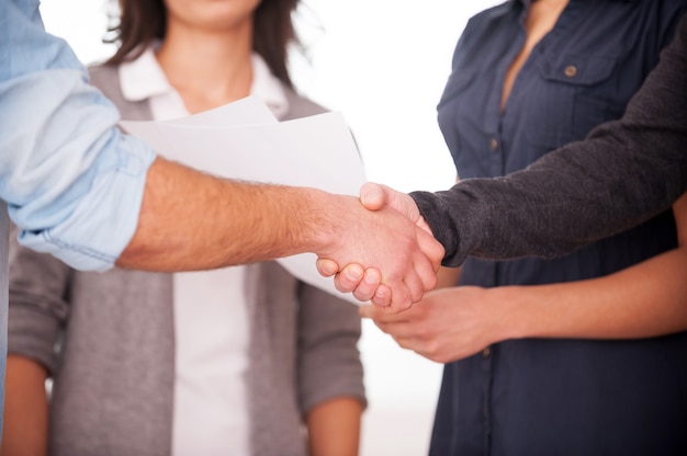 Welkom aan boord! Twee vrolijke jonge mannen handenschudden terwijl twee vrouwen naar hen kijken en glimlachen