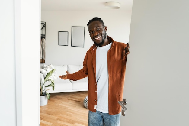 Welkom Gelukkige Afro-Amerikaanse man die bezoeker uitnodigt om zijn huis binnen te gaan in de deuropening van een modern appartement