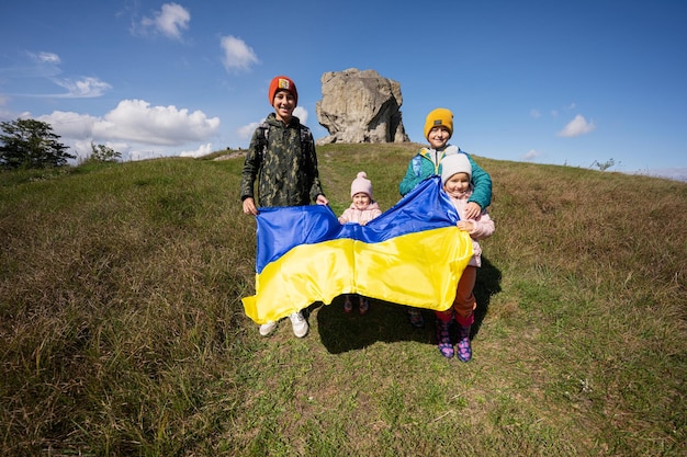 Welkom in Oekraïne Vier kinderen houden Oekraïense vlag vast in de buurt van grote steen in heuvel Pidkamin