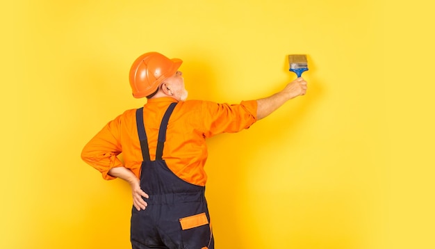 Welkom op mijn plaats schilder in werkende uniform werkende indoor man met schilderborstel workman hand met penseel schilderij buitenkant van gebouw senior man bouwer schilderij gele muur