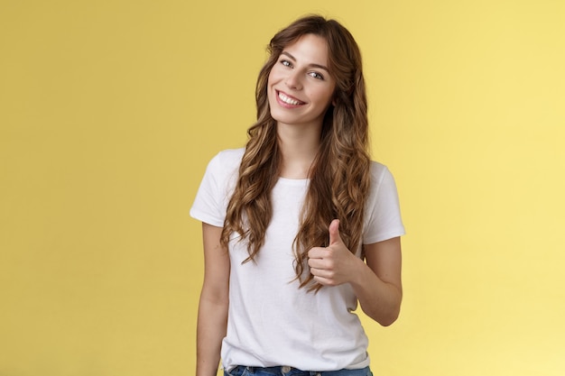 Well done congratulations. Happy charismatic pretty european female tilt head smiling broadly accept agree your idea like satisfied good result show thumb up approval gesture yellow background