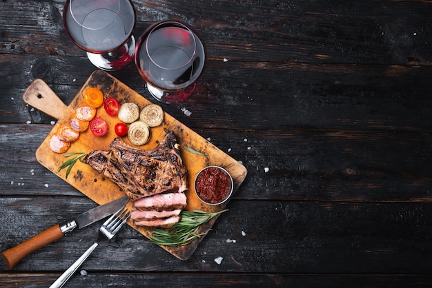 Bistecca di maiale ben cotta su un tagliere. due bicchieri di vino rosso secco. cena per due posti per il testo