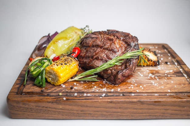 Well done steak with grilled corn, paprika, pepper, onion, garlic and rosemary on wooden board