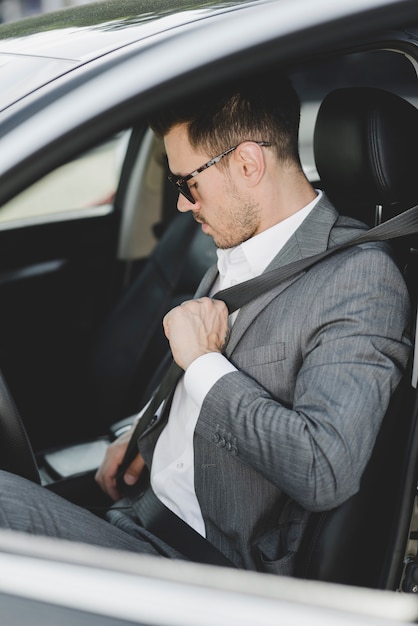 Photo well dressed young man tying safety belt in the car