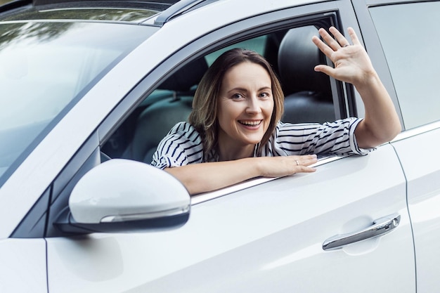 さてこんにちは幸せビジネス女性がカメラを見て車でこんにちはサインを送信します