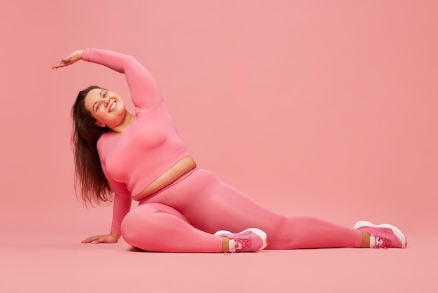 Wellbeing and selflove young overweight woman training in pink sportswear doing stretching against