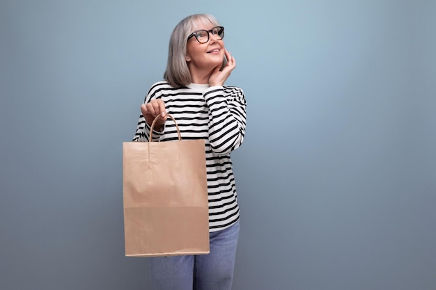 Wellgroomed old woman of the s with purchases in a craft bag on a bright background with copy space