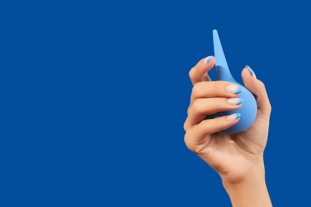 Фото Ухоженная женская рука держит клизму на синем фоне