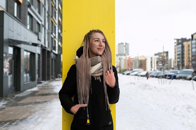 A wellgroomed young woman with blond dreadlocks walks down the street in the cold