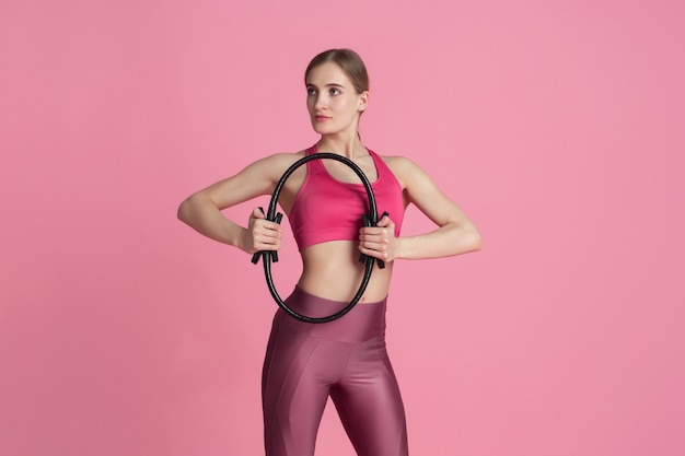 Wellness. Beautiful young female athlete practicing in studio, monochrome pink portrait