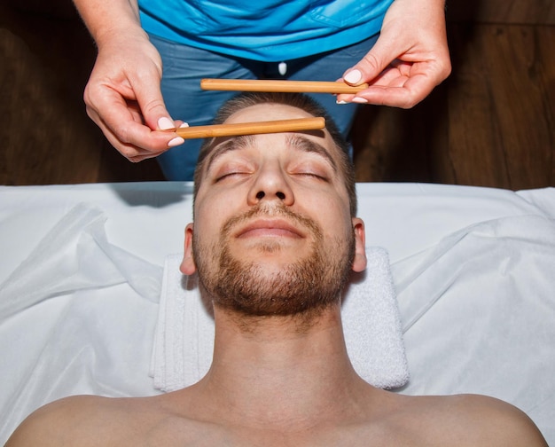 Wellness concept Professional masseur gives a man a Thai facial massage with special sticks in a spa center Relaxation and recovery after work