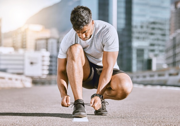 Wellness- en fitnessrunner bindt schoenen veter voordat hij in de zomer in een stadsstraat rent Gezonde man-atleet bereidt sneaker voor op een comfortabele pasvorm voor een sporttraining of marathontraining