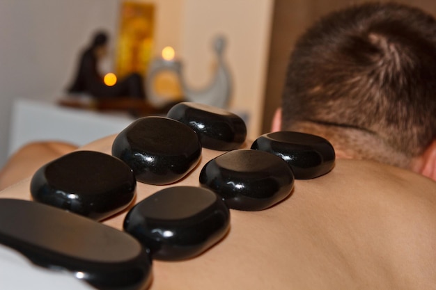 Wellnessconcept Knappe jongeman ontspannend onder het stimulerende effect van een traditionele hotstone-massage in een luxe spa- en wellnesscentrum Herstel na het werk