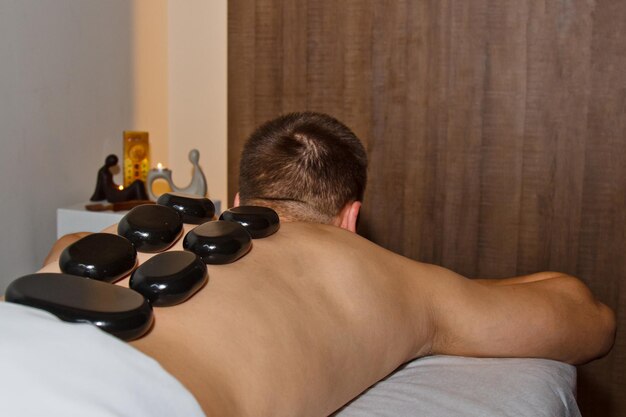 Wellnessconcept Knappe jongeman ontspannend onder het stimulerende effect van een traditionele hotstone-massage in een luxe spa- en wellnesscentrum Herstel na het werk