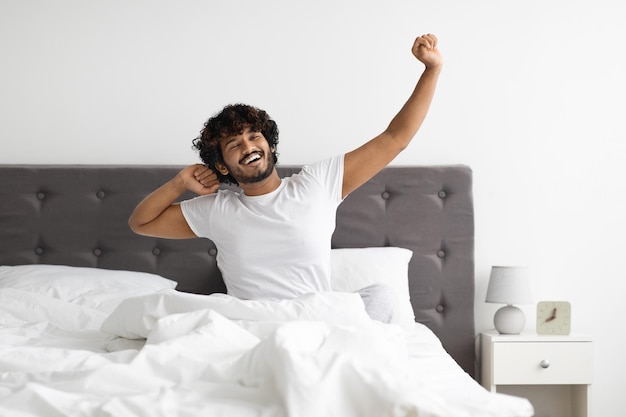 Wellrested indian guy in pajamas stretching in bed