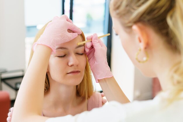 Wenkbrauwmeester tijdens het verwijderen van gezichtshaar met wax Huid- en haarverzorging