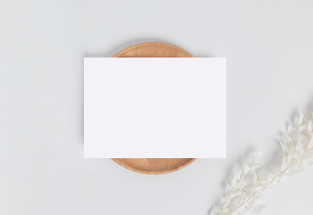 Wenskaart of uitnodigingskaart met witte droge bloembladeren op houten plaat of dienblad in witte achtergrond bovenaanzicht mock-up voor ontwerp