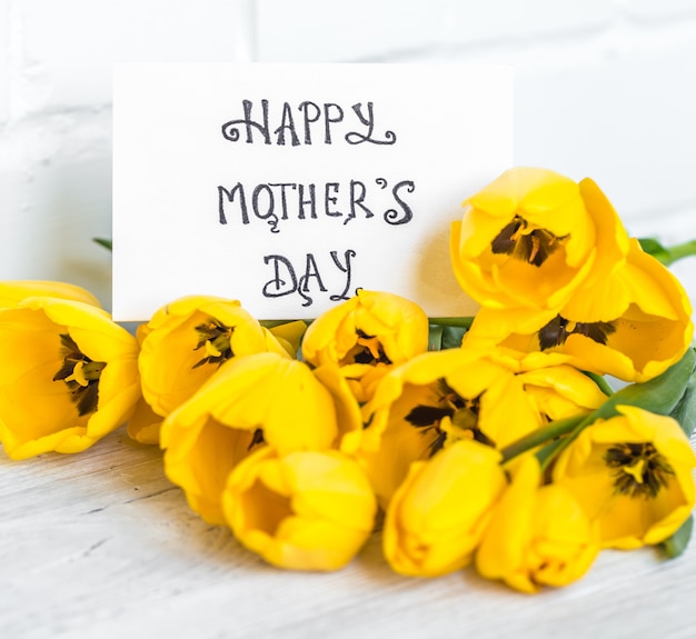 wenskaart voor Moederdag en gele tulpen op houten tafel