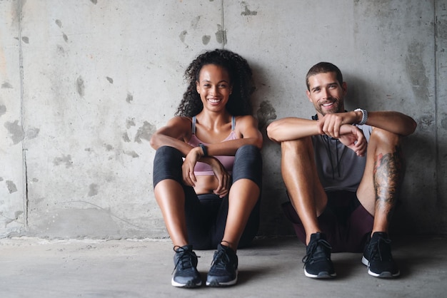 Were down but not out Portrait of a sporty young couple sitting down against a wall while exercising inside a parking lot