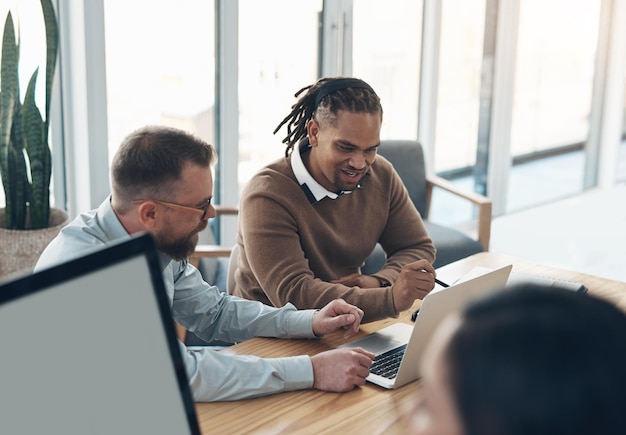 Were getting somewhere with our idea Cropped shot of two handsome businessmen sitting and using a laptop in the office while their colleagues work around them